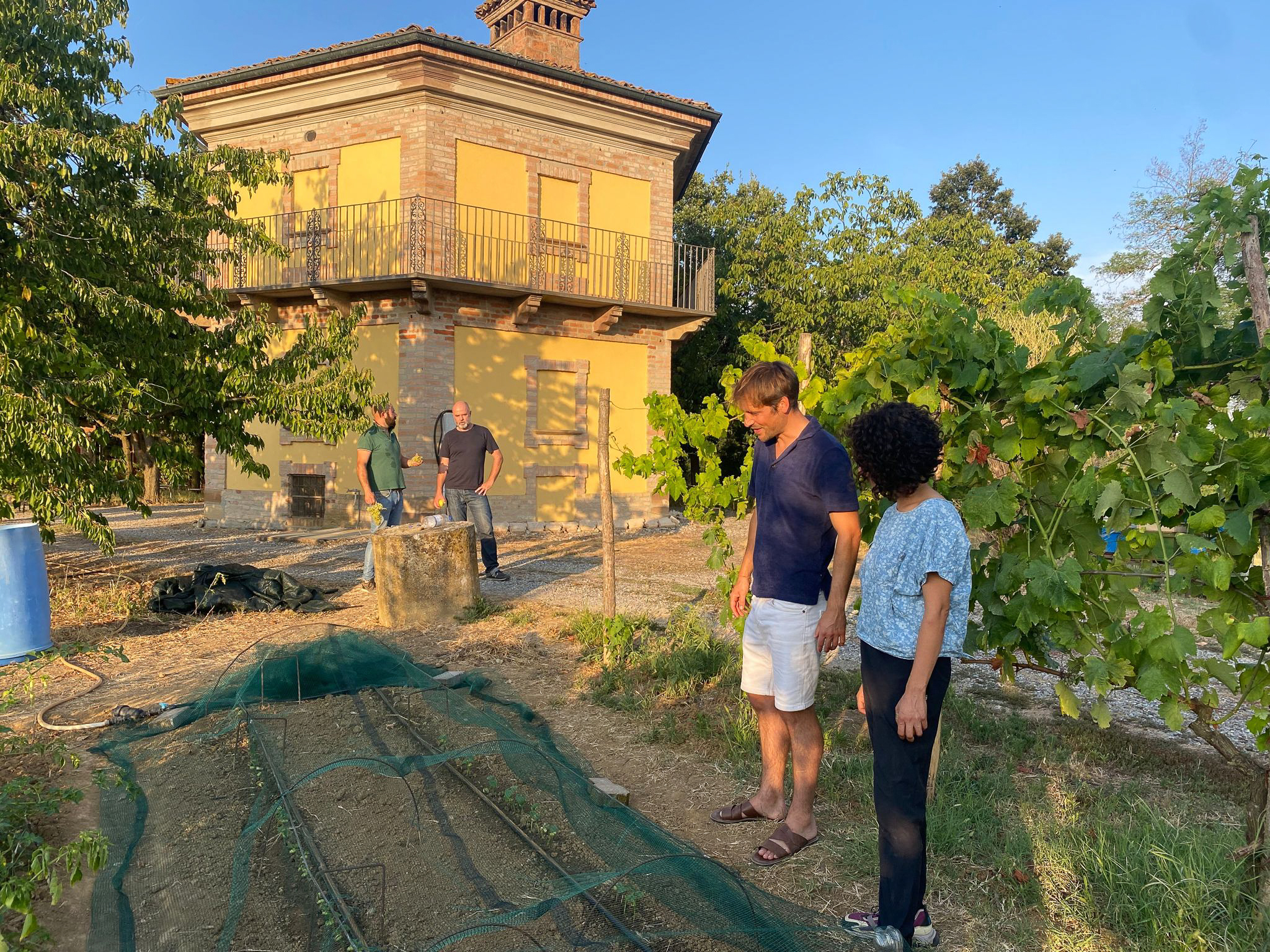 Cascina gialla con piante e persone